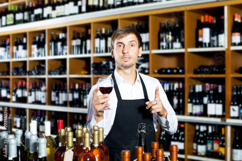 Man seller wearing uniform holding glass of wine