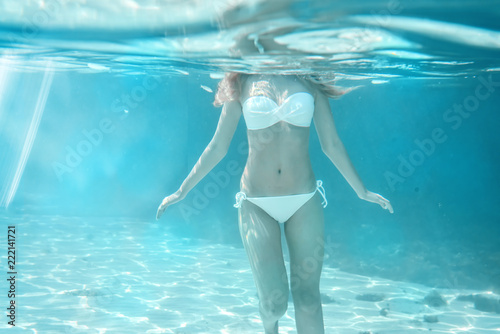 Girl body swimming underwater portrait. Sea summer blue water background with bubbles sunny ray of lights