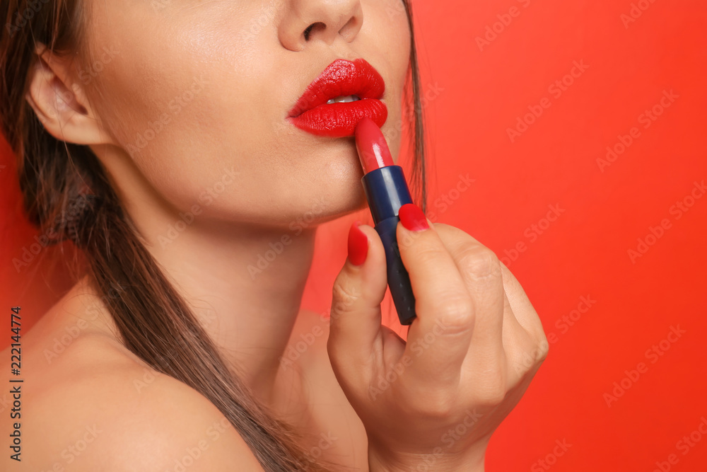 Beautiful young woman applying red lipstick on color background, closeup Beautiful young woman applying red lipstick on color background, closeup