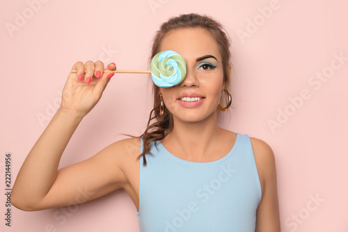 Beautiful young woman with pink lipstick and lollipop on color background
