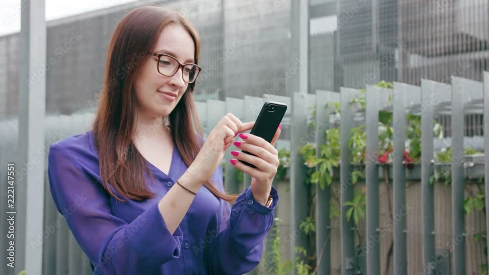 A happy smiling brunette woman with glasses using a phone in the city street. Medium shot. Soft focus A happy smiling brunette woman with glasses using a phone in the city street. Medium shot. Soft focus