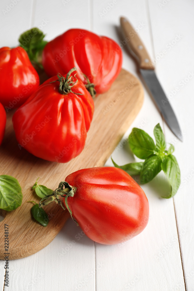 Board with delicious tomatoes and fresh basil on white wooden table Board with delicious tomatoes and fresh basil on white wooden table