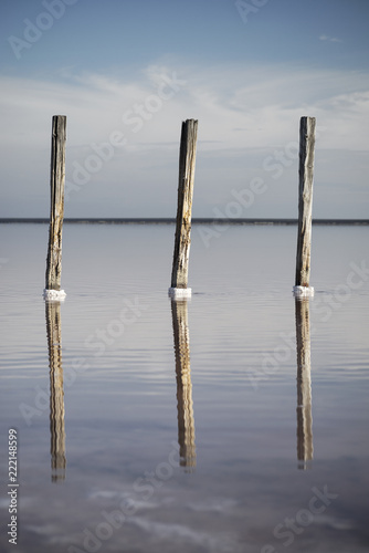 three wooden columns in water with reflections in red salt lake in Ukraine
