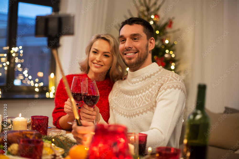 christmas, holidays, technology and people concept - happy couple in taking picture by selfie stick at home dinner