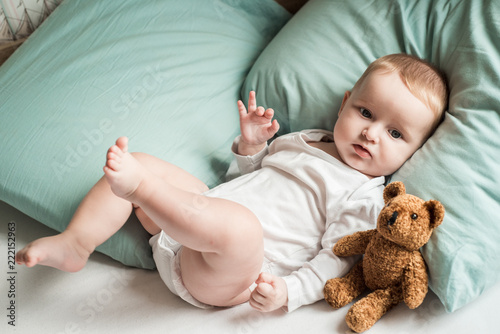 sleeping boy.Lovely blond baby in a bed in the morning before going to bed, a toy bear teddy. He laughs and plays with a foot.