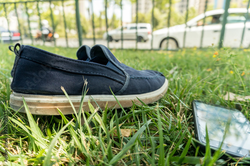 Pair of sports shoes on grass field and cellphone.