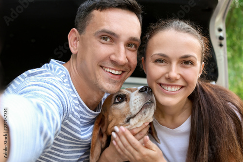 Young couple with cute dog taking selfie near car outdoors