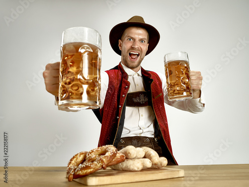 Germany, Bavaria, Upper Bavaria. The young happy smiling man with beer dressed in traditional Austrian or Bavarian costume holding mug of beer at pub or studio. The celebration, oktoberfest, festival photo