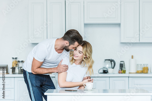 happy young couple embracing during breakfast in kitchen