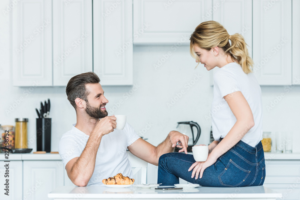 happy young couple drinking coffee and smiling each other at morning happy young couple drinking coffee and smiling each other at morning