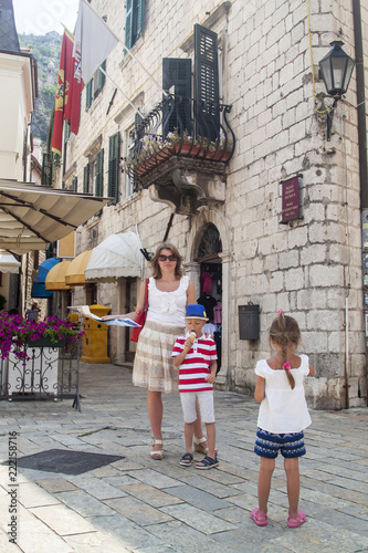 concept of travelling with children. beautiful woman holding a travel guide next to her children stand on the square of the old town of Kotor, Montenegro © sommersby