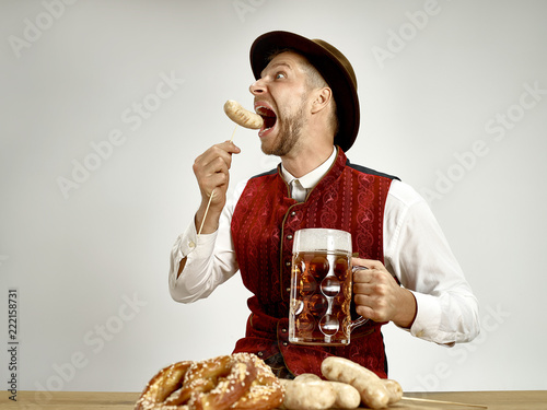 Germany, Bavaria, Upper Bavaria. The young happy smiling man with beer dressed in traditional Austrian or Bavarian costume holding mug of beer at pub or studio. The celebration, oktoberfest, festival