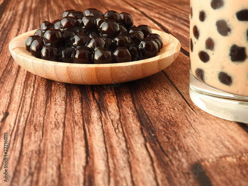 A glass cup of pearl milk tea (also called bubble tea) and a plate of tapioca ball on wooden background. Pearl milk tea is the most representative drink in Taiwan. Taiwan food . With copy space.