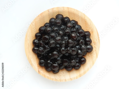 Top view of tapioca ball (also known as boba in bubble tea) on wooden plate isolated on white background. It is ingredients for making pearl milk tea and shaved ice at dessert shop. Food concept.