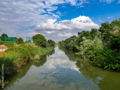 Henares river on its way through the city of Alcala de Henares in Spain with very green banks and a sky with clouds photo