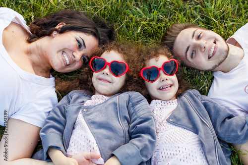 Children with parents in the park. Cute family haming fun in nature. Twin toddler sisters holding parents. Happy family concept