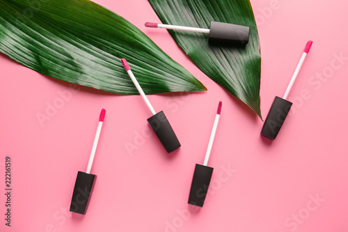Brushes with lipstick and tropical leaves on color background photo