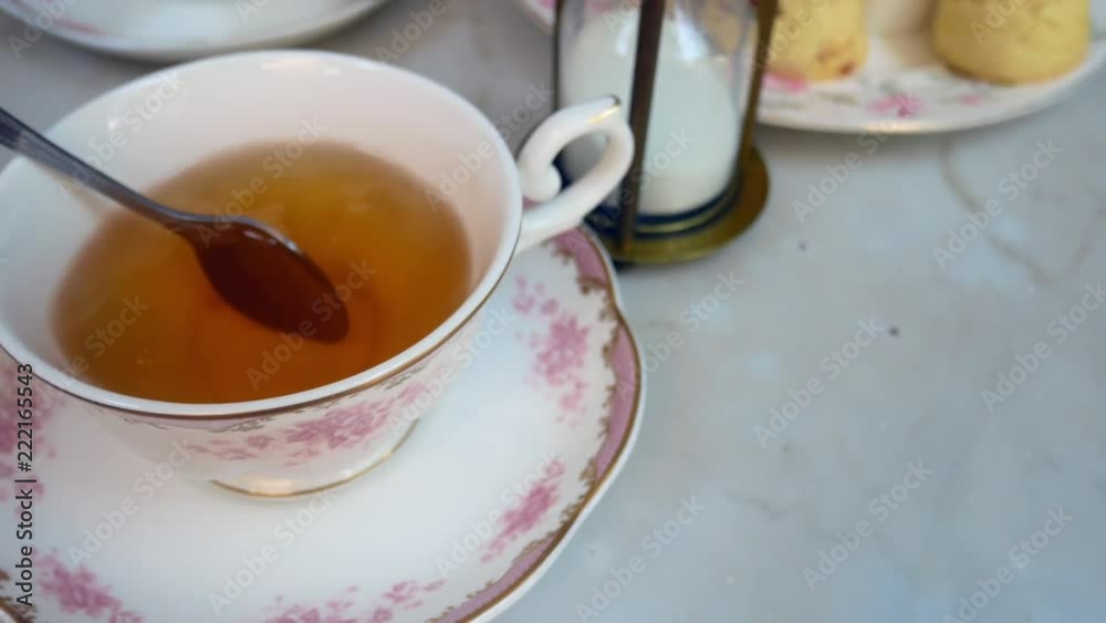 Hand is using stainless steel to stir english tea in the beautiful english tea cup with background of sweet dessert (scone) Hand is using stainless steel to stir english tea in the beautiful english tea cup with background of sweet dessert (scone)