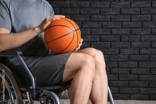 Young basketball player sitting in wheelchair against dark brick wall