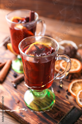 Glass cups of delicious hot mulled wine on wooden board