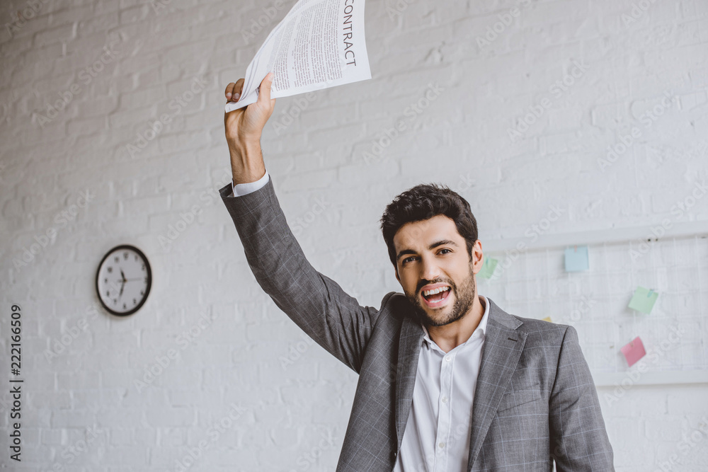 happy handsome businessman holding documents in raised hand in office happy handsome businessman holding documents in raised hand in office