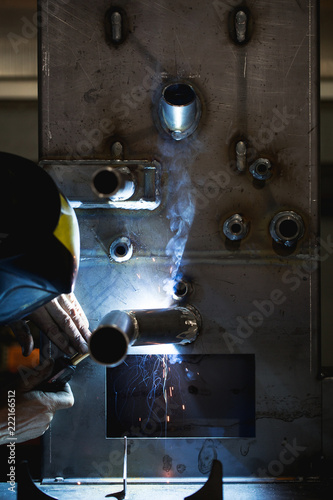 Metallurgy industry. Factory for production of heavy pellet stoves and boilers. Close up of manual worker welder on his job. Extremely dark conditions and visible noise. photo