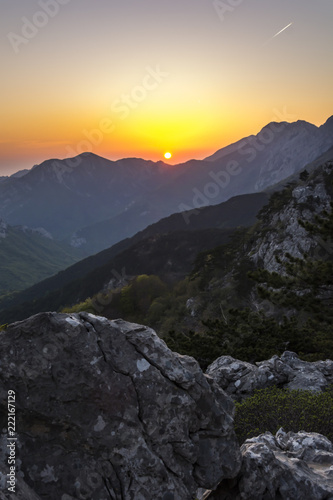 Amazing sunset above great mountains "Paklenica" in Croatia. The orange sun near the horizon. Illuminating mountains and rocks by sun. Beautiful view on sunset landscape.