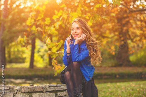 Fototapeta Naklejka Na Ścianę i Meble -  Cute young woman using smartphone in the park with autumn season colors.