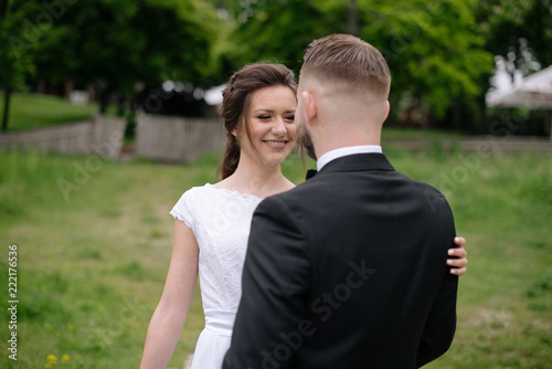 Beautiful smiling bride woman in white wedding dress looking at the groom. Outdoors in the green park. Wedding day concept