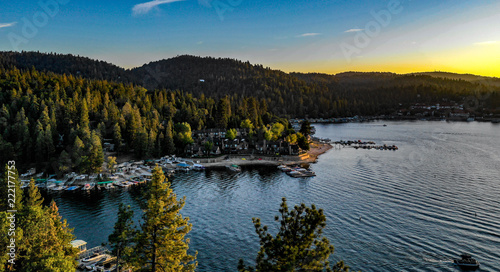 Aerial sunset view of Lake Arrowhead with blue water, green trees, boats, golden clouds, yellow, red, orange, blue, pink, purple colors