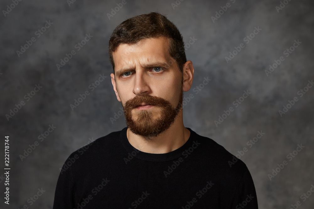 Picture of annoyed adult bearded male frowning, being irritated with something, expressing bad negative emotions, staring at camera. Human facial expressions, reaction, feelings and attitude