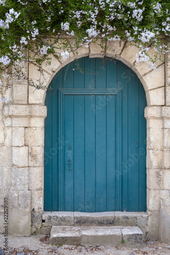 Old blue green door in a stone wall with flowers above. © florent