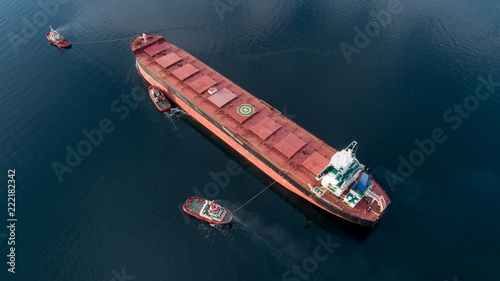 Aerial shot of a cargo ship approaching port with help of towing ship