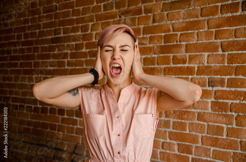 Young beautiful girl closed ears with opened mouth on a brick wall background