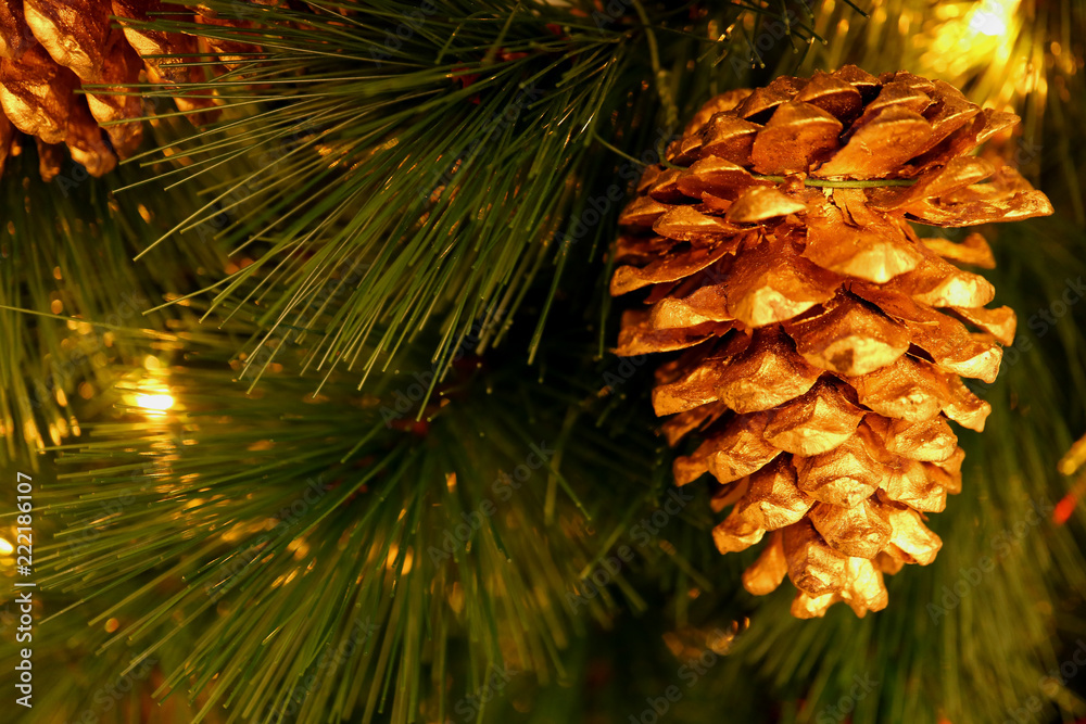 Shiny gold colored dry pine cone ornament hanging on sparkling Christmas tree 
