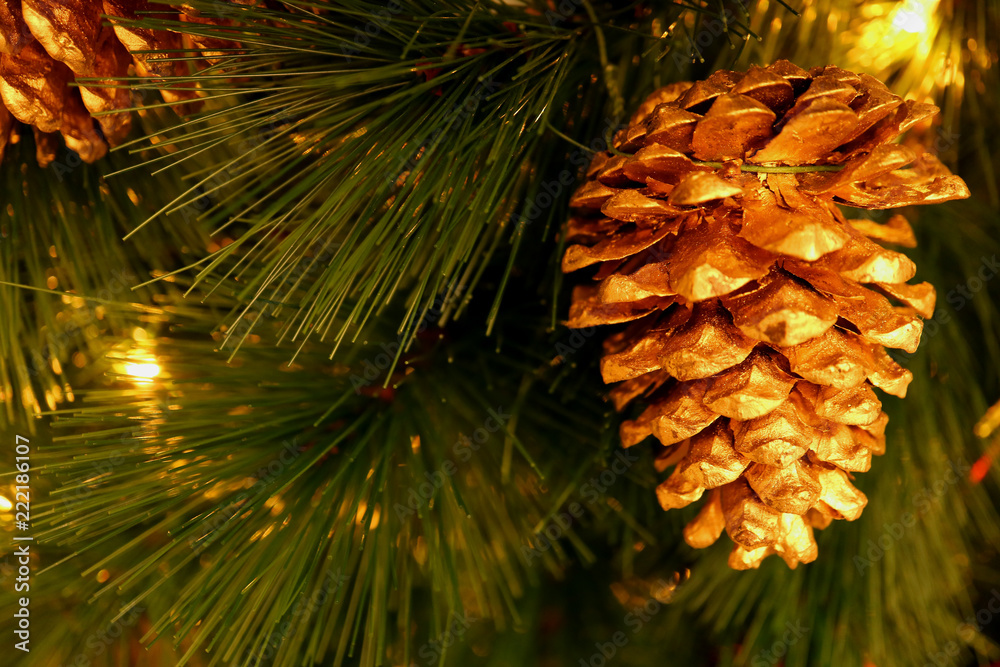 Fototapeta premium Shiny gold colored dry pine cone ornament hanging on sparkling Christmas tree