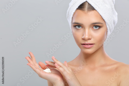 Beautiful young woman with perfect skin with a towel on her head, isolated on a gray background.