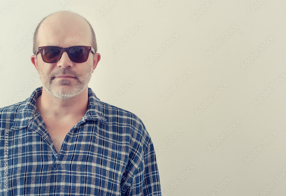 Portrait of an adult man with a gray beard with dark glasses shirt on a light background, toned. Portrait of an adult man with a gray beard with dark glasses shirt on a light background, toned.