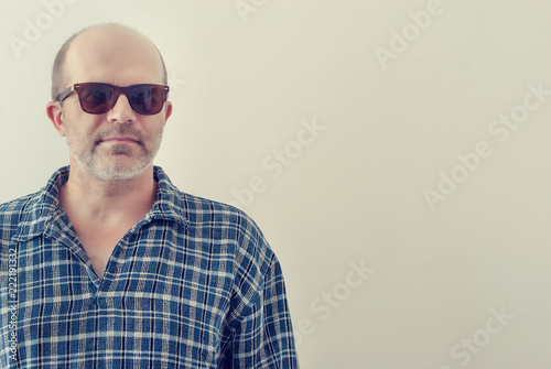 Portrait of an adult man with a gray beard with dark glasses shirt on a light background, toned.
