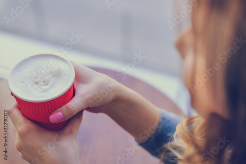 Concept of having a cup of coffee in the morning. Young lady is gossiping with her best friend in a cafe while drinking frothy coffee. Close up photo of coffee with foam. Top, overheadview photo