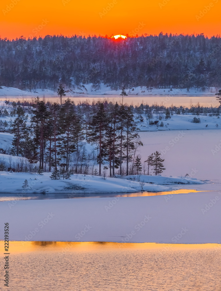 A colorful sunset on the Ladoga lake in the frost. Winter day. Open water hovers from frost. Islands in the snow.