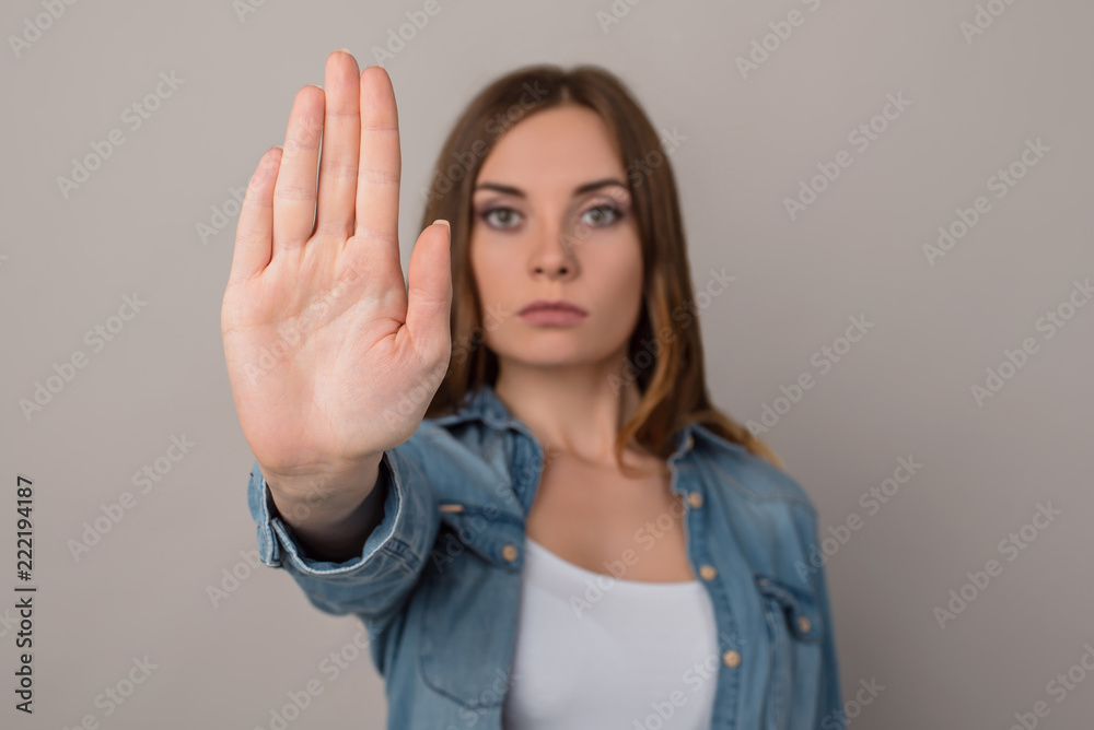 Close up cropped photo of hand making showing demonstrating a sign stop with a hand, serious concentrated face, isolated on gray background, copy space Close up cropped photo of hand making showing demonstrating a sign stop with a hand, serious concentrated face, isolated on gray background, copy space