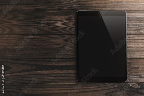Black tablet computer on wooden brown background with space for text, light effect