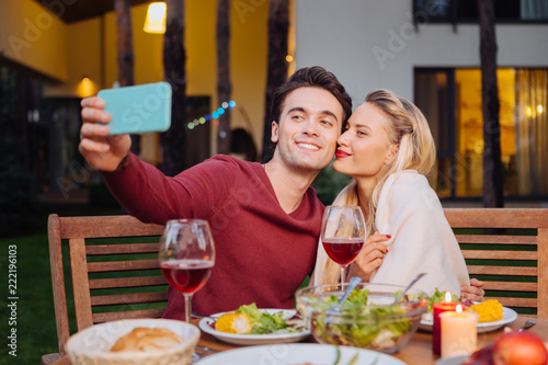 Our photo. Joyful nice man smiling while taking a selfie with his girlfriend in the restaurant