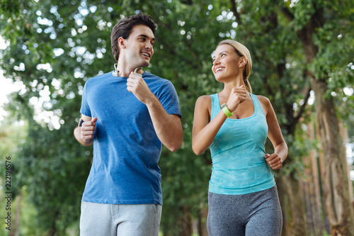 Outdoor activity. Nice healthy couple smiling while jogging together in the wood