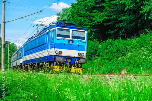 A blue electric locomotive passing the Czech countryside. A train running through the green valley. Rail transport in the Czech Republic