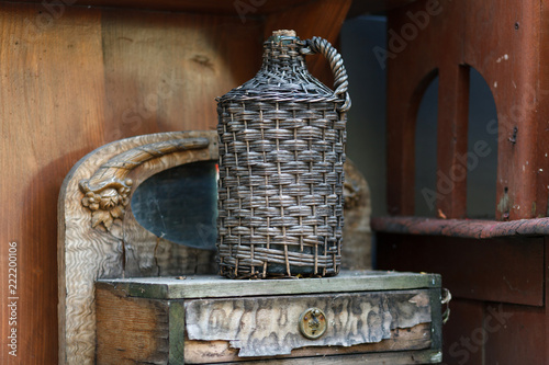 Bild auf Leinwand Carboy in wicker basket on wooden table