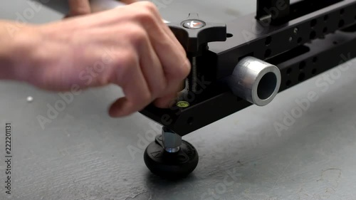 Male hand adjusting a levelling foot on a a camera dolly slider clamp holding speed rail. photo