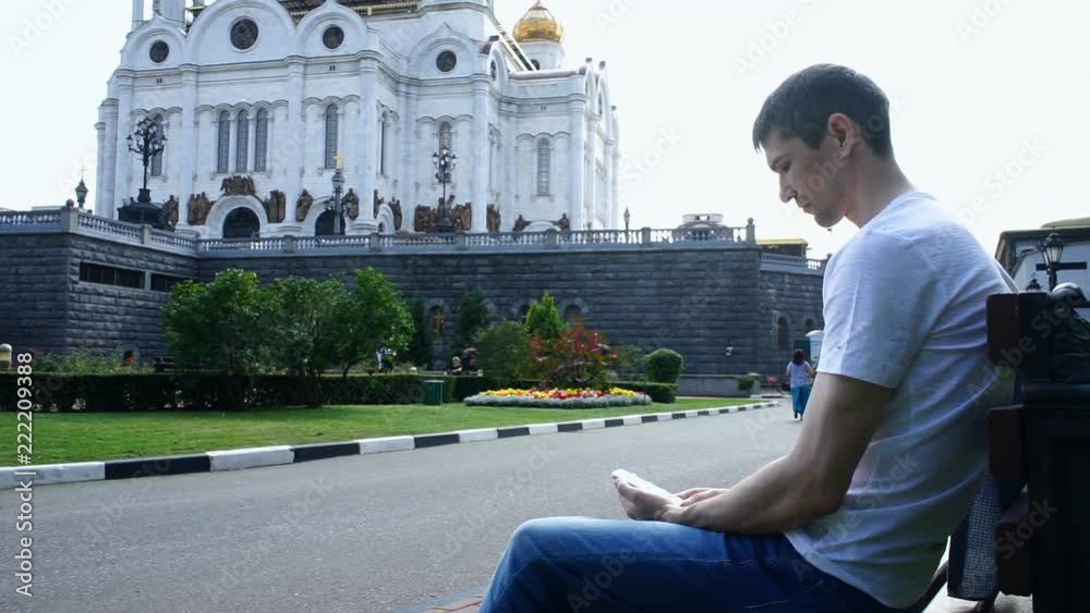 Man is sitting with a phone near the church Man is sitting with a phone near the church