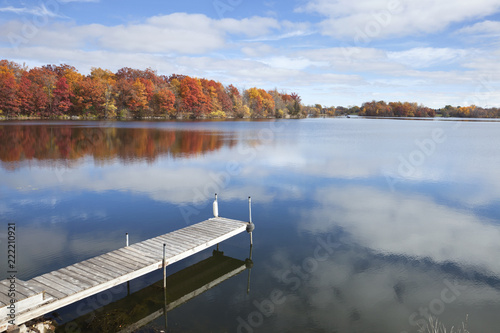 Fototapeta Naklejka Na Ścianę i Meble -  Minnesota lake and dock with trees in full autumn color, blue sky and clouds
